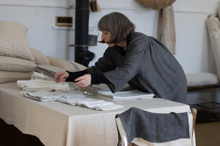 Rustic striped grainsack fabric roll and piles in a workroom with the maker