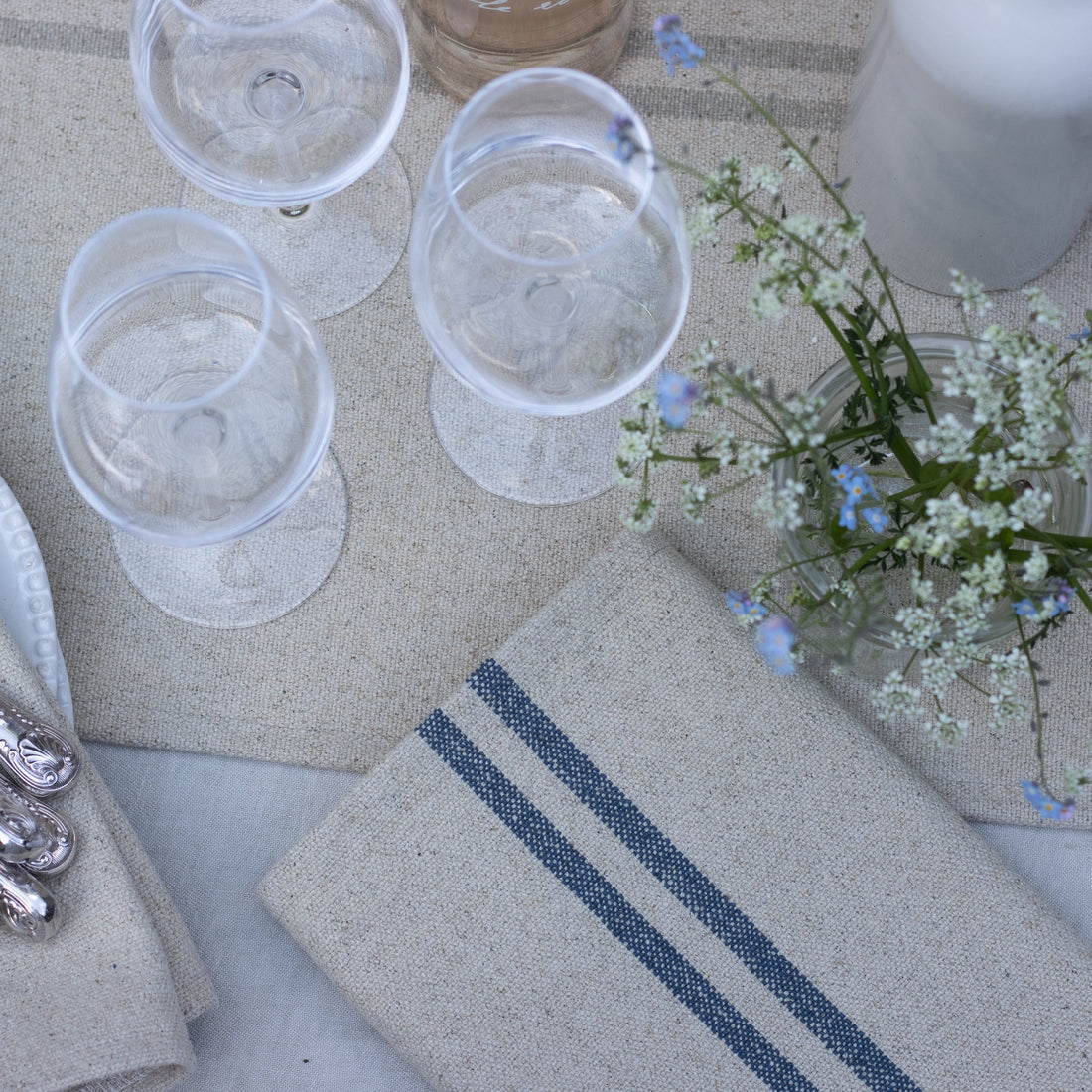 Table setting with glasses, napkins, and a small floral arrangement on a textured surface.