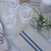 Table setting with glasses, napkins, and a small floral arrangement on a textured surface.