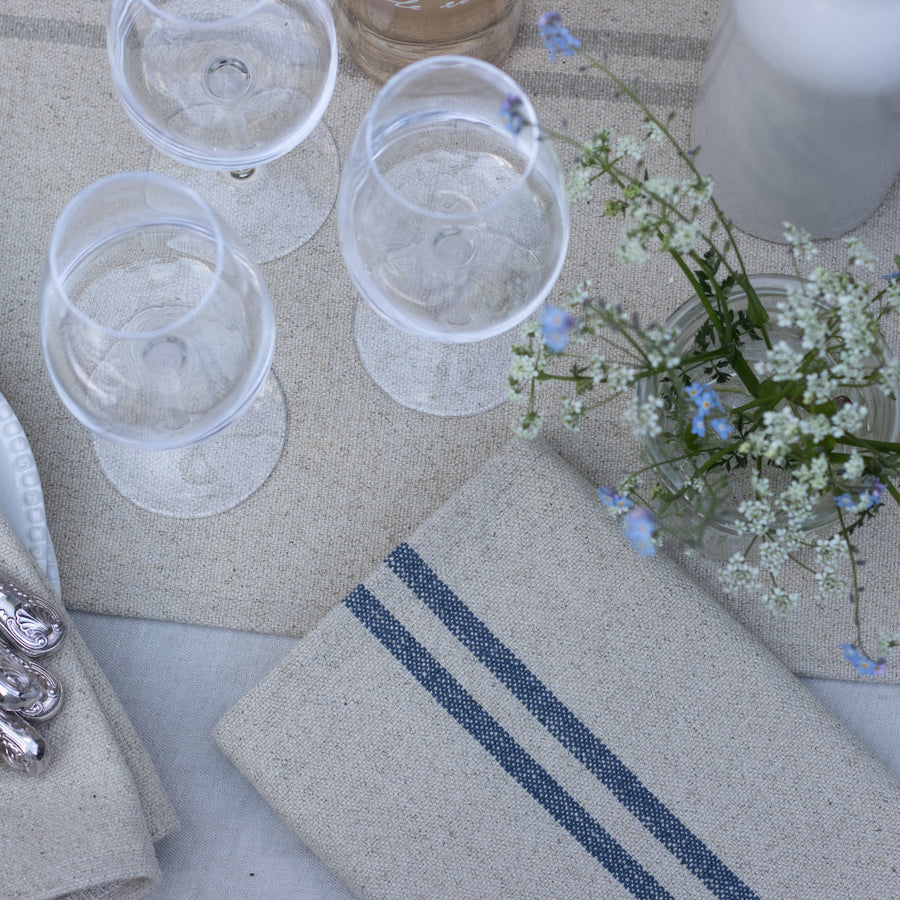 Table setting with glasses, napkins, and a small floral arrangement on a textured surface.
