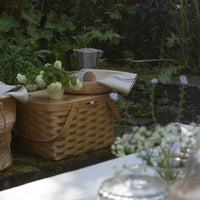Outdoor setting with a picnic basket, flowers, and a glass container on a table.