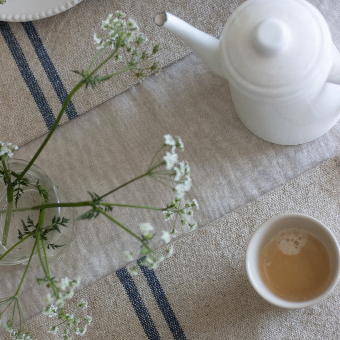 Tea set with a teapot, cup, and saucer on a tablecloth with a striped pattern.