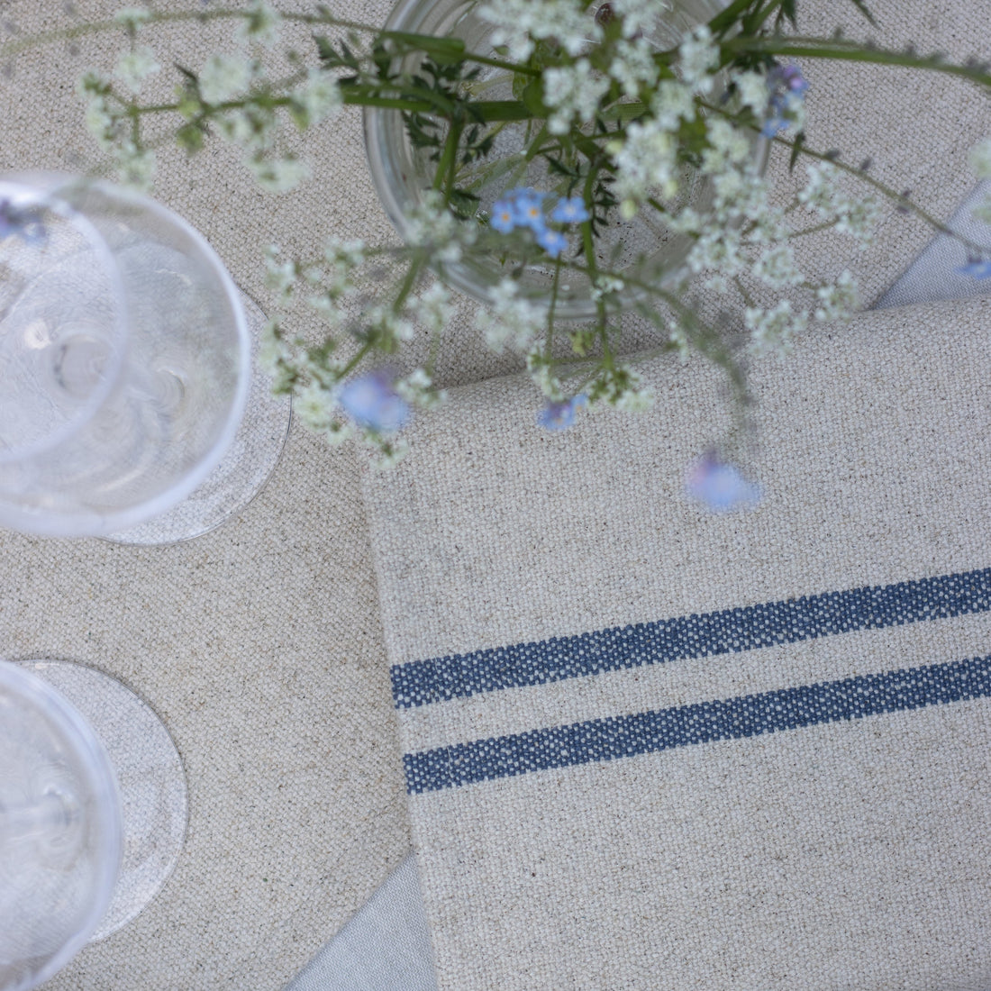 Table setting with a striped napkin, glasses, and a vase of flowers on a textured surface.