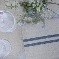Table setting with a striped napkin, glasses, and a vase of flowers on a textured surface.