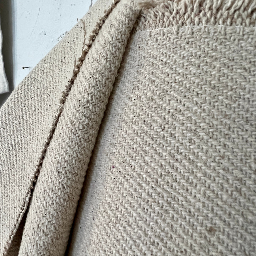 A close-up view of a cream rustic cotton twill fabric with a textured pattern.